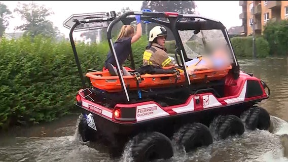 Ein Mann wird aus einem Hochwassergebiet gefahren. © Westküstennews 