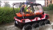 Ein Mann wird aus einem Hochwassergebiet gefahren. © Westküstennews 
