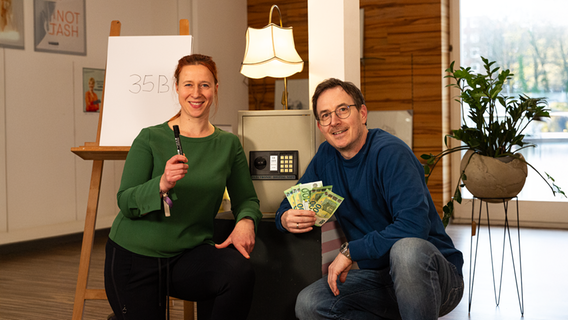 Mandy Schmidt und Horst Hoof des NDR1 vor einem Tresor. Horst hält einige Hunderteuroscheine hoch. Auf einer Leinwand steht "35B" geschrieben. © NDR Foto: Dominik Duehrsen