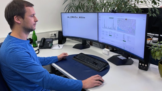 Ein Mann in einem blauen Pulli sitzt an einem Arbeitstisch mit zwei PC-Monitoren. © NDR Foto: Lena Haamann