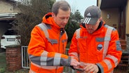 Zwei Mitarbeiter von der Stadtentwässerung Wedel blicken auf ein Handy. © NDR Foto: Lena Haamann