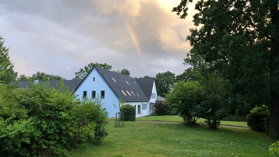Ein Haus steht auf einer Wiese, im Hintergrund ist ein Regenbogen © NDR Foto: Nadina von Studnitz