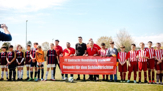 Schiedsrichter Pascal Martin posiert mit Vereinsmitgliedern und Fußballspielern vor einem Plakat, das für Respekt für Schiedsrichter wirbt. © NDR Foto: Lisa Pandelaki