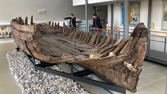 Zwei Männer stehen hinter dem Uelvesbüller Wrack im Husumer Schifffahrtsmuseum in Nordfriesland. © NDR Foto: Astrid Cohrs-Dreessen