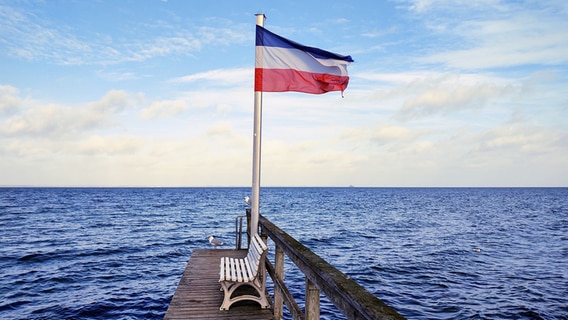 Ein Steg an der Ostsee mit Sitzbank und wehender Flagge. © Marion Ostermann Foto: Marion Ostermann
