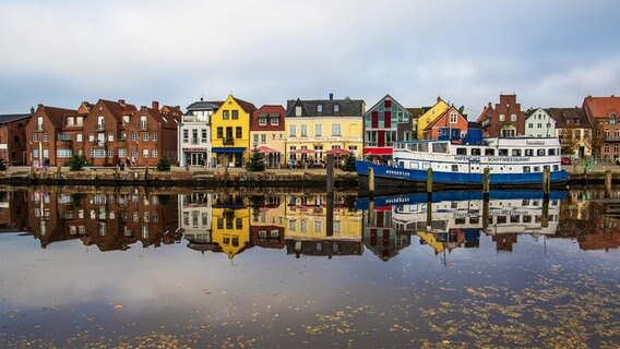 Die bunten Häuser von Husum spiegeln sich im Hafenbecken. Auch ein Schiff liegt im Hafen und wird gespiegelt. © Rolf Brückner Foto: Rolf Brückner