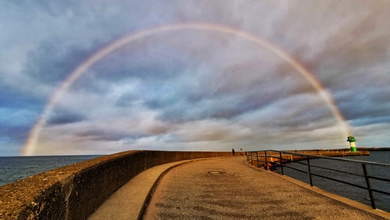 Ein Regenbogen erstreckt sich über das gesamte Bild. Links und rechts Wasser, in der Mitte ein Weg zum grünen Leuchtturm. © Nicole Rankovic Foto: Nicole Rankovic