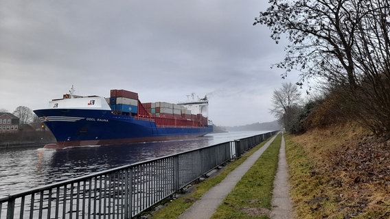 Unter bewölktem Himmel fährt ein großes Containerschiff durch den Nord-Ostsee Kanal. © Marita Volkmann Foto: Marita Volkmann
