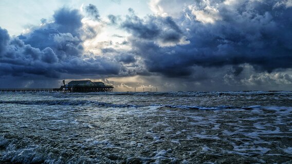 Stelzenhäuser am Strand der Nordsee bei dunklen Wolken und stürmischem Meer. © Achim Otto Foto: Achim Otto