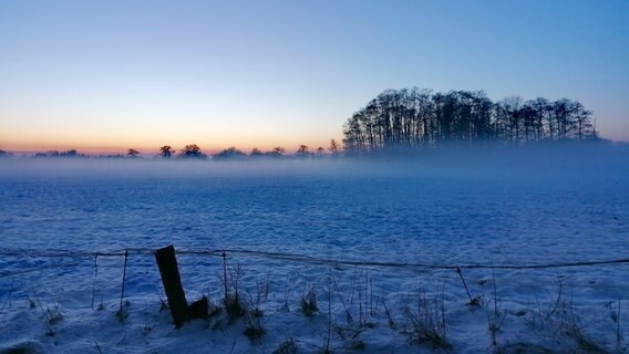 Sonnenuntergang über einem mit Schnee bedeckten Feld im Nebel. © Anja Janda Foto: Anja Janda