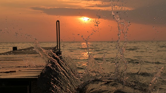 Ein Badesteg bei Sonnenaufgang, rechts spritzt Wasser hoch. © Melanie Lettau Foto: Melanie Lettau