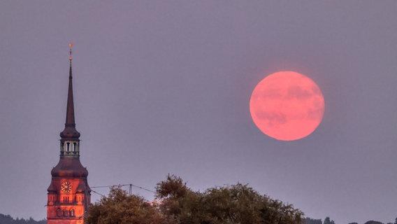 Der rote Supermond steht am Himmel hinter einer Kirche in Itzehoe. © Frank Kossiski Foto: Frank Kossiski