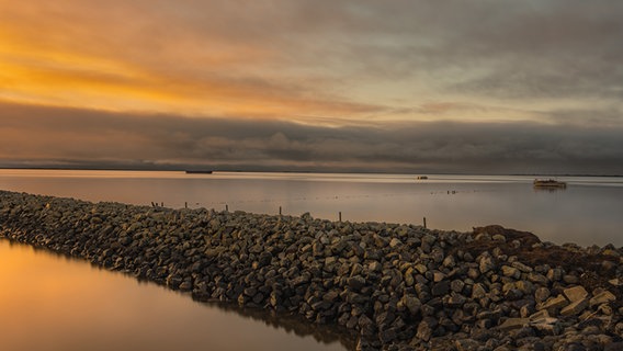 Eine Steinmole in Schlüttsiel im Sonnenuntergang mit Blick auf die Nordsee. © Peter Kuhr Foto: Peter Kuhr