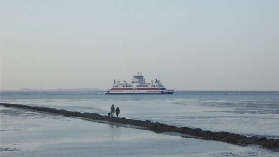 Eine Familie steht im Wattenmeer und betrachtet eine Fähre in der Ferne. © Cordula Sönnichsen Foto: Cordula Sönnichsen