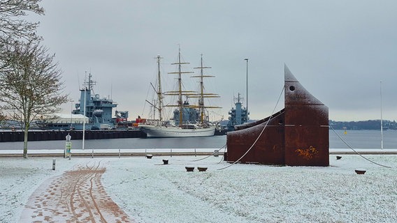 Die Stahlplastik "Hafen 77" mit Schnee bedeckt, im Hintergrund die Gorch Fock am Marinehafen. © Melanie Volkmann Foto: Melanie Volkmann