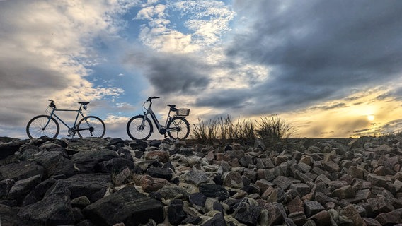 Zwei Fahrräder stehen bei Sonnenuntergang auf einem Steindamm bei Heiligenhafen. © Olaf Gülzow Foto: Olaf Gülzow