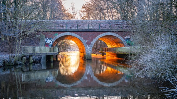 Das Morgenlicht fällt durch die Tunnel der Bahnüberführung in Bad Schwartau und spiegelt sich im Wasser. © Karin Bräunert Foto: Karin Bräunert