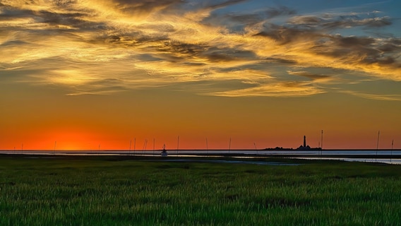 Am Horizont fährt ein Krabbenkutter bei Sonnenuntergang in den Tümlauer Hafen ein. © Claus Carstens Foto: Claus Carstens