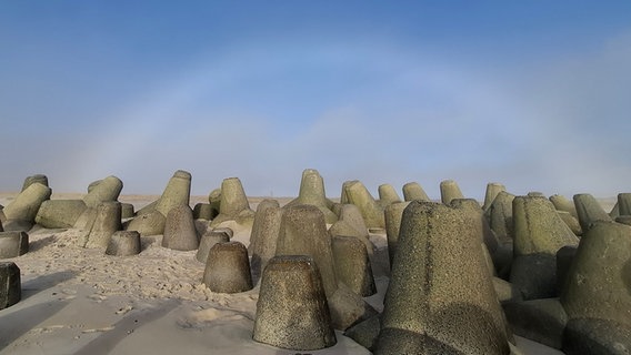 Über den Tetrapoden am Strand erscheint ein weißer Nebelbogen. © Dörte Kruse Foto: Dörte Kruse