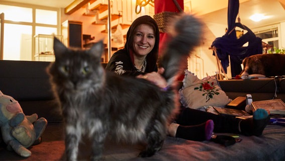 Eine junge Frau mit Kapuzenpullover streichelt auf dem Sofa eine Katze. © Tim Oehler Foto: Tim Oehler