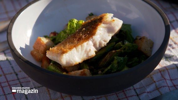 Auf einem Teller ist ein Stück Fisch auf einem Salat drapiert © NDR Foto: NDR Screenshot