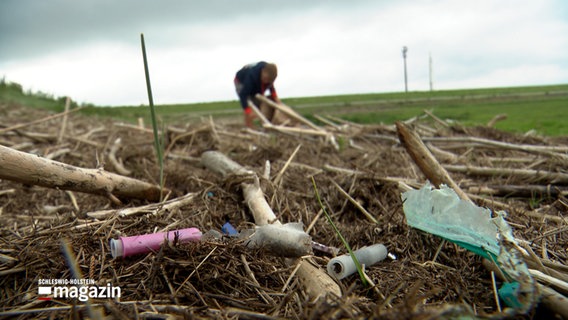 Eine Person sammelt Plastikmüll auf einem Deich, im Vordergrund liegen mehrere Plastikteile © NDR Foto: NDR Screenshot