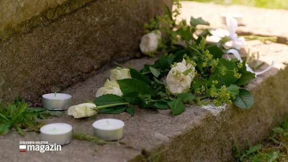 Zum Gedenken an einer im Einsatz getöteten Polizisten liegen weiße Blumen auf einem Stein © NDR Foto: NDR Screenshot