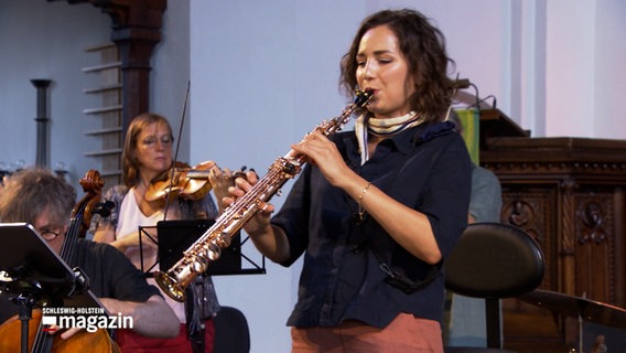 Eine Saxofonistin spielt ihr Instrument zusammen mit einer Band in einer Kirche © NDR Foto: NDR Screenshot