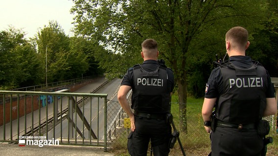 Zwei Polizisten stehen auf einer Brücke und Kontrollieren die Geschwindigkeit einiger Fahrzeuge © NDR Foto: NDR Screenshot