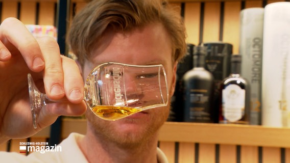 Ein Mann hält ein Whisky-Glas schräg um die Qualität zu überprüfen © NDR Foto: NDR Screenshot