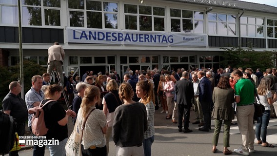 Mehrere Menschen stehen vor einem Haus, an dem Haus ist ein transparent aufgehängt, darauf steht: "Landesbauerntag" © NDR Foto: NDR Screenshot