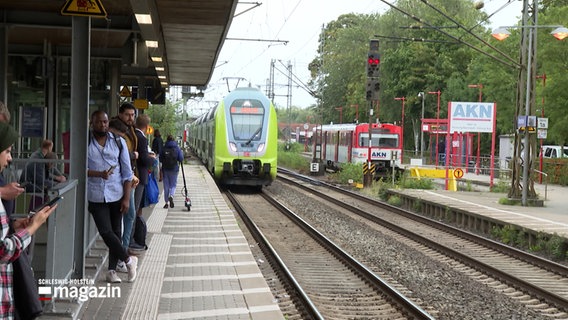 Personen warten auf einem Bahnsteig auf einen einfahrenden Zug © NDR Foto: NDR Screenshot