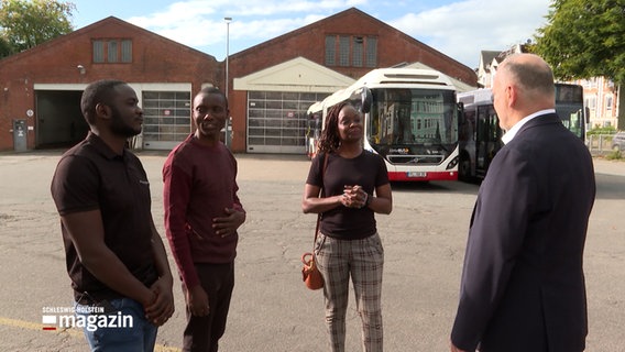 Drei zukünftige Busfahrer stehen vor einem Busdepot © NDR Foto: NDR Screenshot