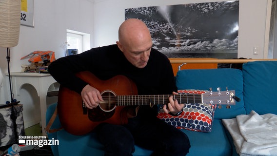 Ein mann sitzt auf einem Sofa und spielt Gitarre © NDR Foto: NDR Screenshot