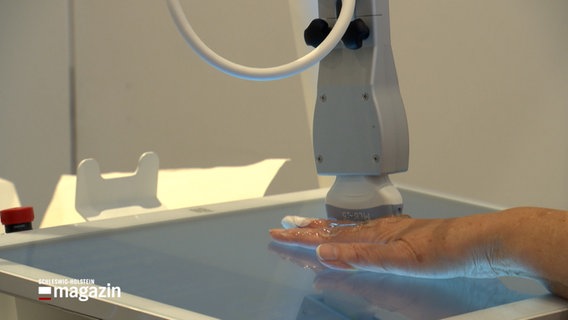 Ein Roboterarm scannt per Ultraschall die Hand eines Menschen © NDR Foto: NDR Screenshot