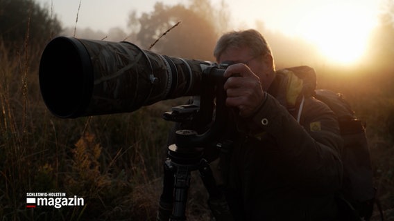 Ein Naturfotograf in Tarnkleidung mit einer Kamera © NDR Foto: NDR Screenshot