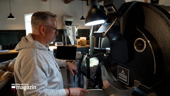 Ein Mann steht vor einer Röstmaschine für Kaffee und beobachtet den Röstvorgang © NDR Foto: NDR Screenshot