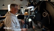 Ein Mann steht vor einer Röstmaschine für Kaffee und beobachtet den Röstvorgang © NDR Foto: NDR Screenshot