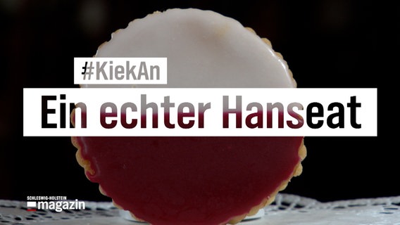 Ein rot-weißer Keks steht aufrecht auf einem Tisch, davor eine Texttafel: "#KiekAn - Ein Echter Hanseat" © NDR Foto: NDR Screenshot