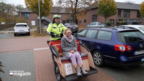 Eine Frau wird von einem Mann in einer Rikscha über einen Parkplatz gefahren © NDR Foto: NDR Screenshot