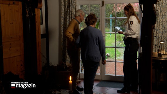 Eine Polizistin im Gespräch mit zwei Personen in einem Haus © NDR Foto: NDR Screenshot