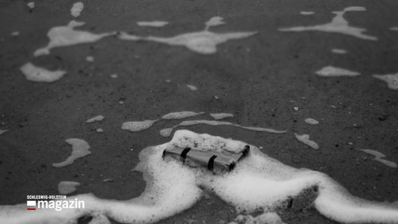 Eine Schwarzweiß-Aufnahme zeigt ein angeschwemmtes Päckchen an einem Strand © NDR Foto: NDR Screenshot