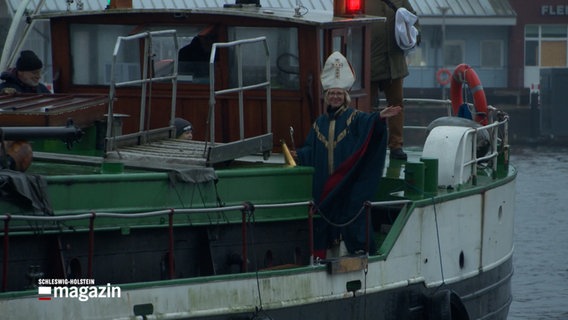 Eine Frau in einem Nikolauskostüm winkt von einem Schiff aus Kindern zu © NDR Foto: NDR Screenshot