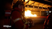 Ein Feuerwehrmann steht vor einer Gruppe von Einkaufswagen, die in Brand geraten sind. © NDR Foto: NDR Screenshot