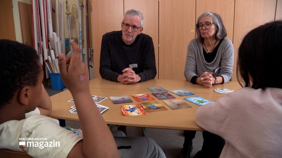 Schüler einer Grundschule im Gespräch mit zwei Senioren in einem Klassenzimmer © NDR Foto: NDR Screenshot