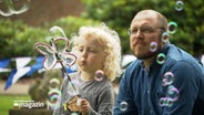 Ein kleines Mädchen erzeugt im Beisein ihres Vaters Seifenblasen. © NDR 