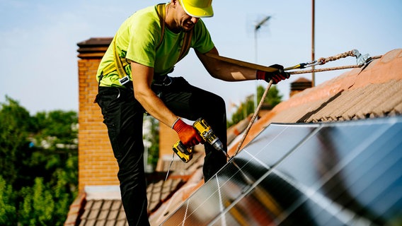 Ein Monteur fixiert ein Solarpanel auf einem Dach © picture alliance / Westend61 Foto: Jake Jakab