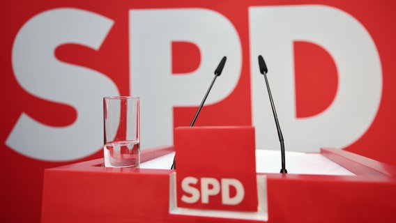 Das Podium mit Parteilogo, Mikrofon und einem deutlich geleerten Wasserglas in der Parteizentrale der SPD. © picture alliance Foto: Hannes Albert/dpa