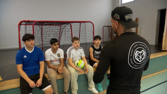 Jugendliche haben in einer Turnhalle eine Besprechung mit dem Trainer. © NDR 