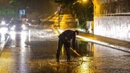 Ein Polizist versucht mit einer Schaufel einen Regenwasserabfluss auf einer Straße in Flensburg zu befreien. © nordpresse mediendienst/Sebastian Iwersen Foto: Sebastian Iwersen